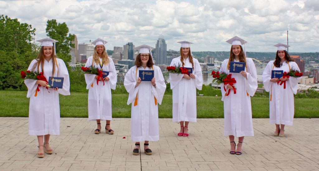 Students standing in a park overlooking the city in their graduation gowns holding their diplomas after graduating from the Notre Dame Academy catholic all-girls school in Covington, Northern Kentucky.