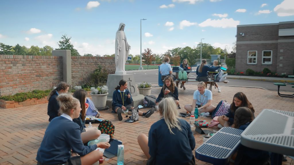 Students sitting outside eating lunch around the statue of the Virgin Mary at the main entrance to the school at the Notre Dame Academy catholic all-girls school in Covington, Northern Kentucky.