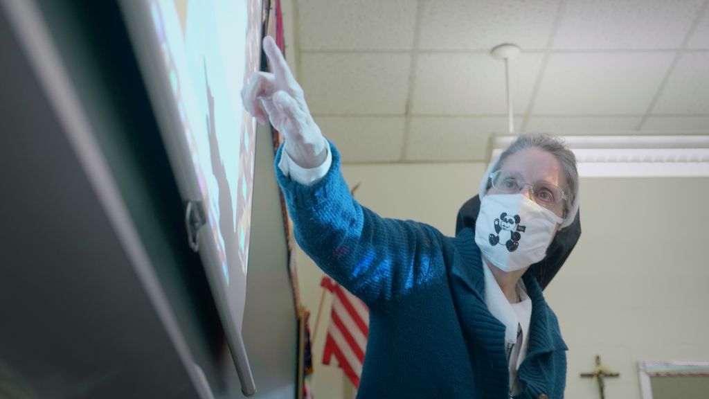 A teacher wearing a face mask leaning towards the white board pointing out information to her students at the Notre Dame Academy catholic all-girls school in Covington, Northern Kentucky.